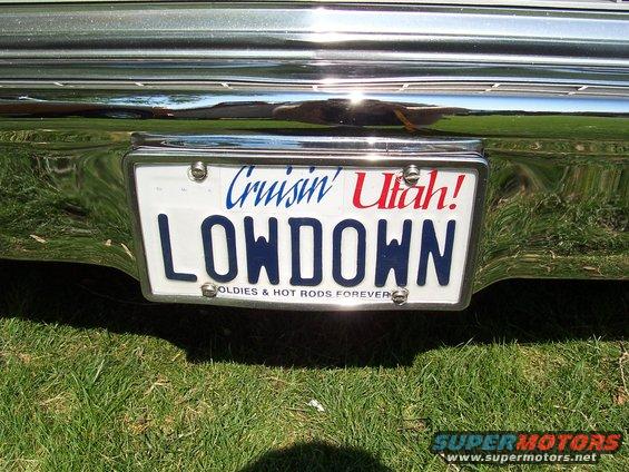 License plate frame with 'Cruisin' Utah!' and 'LOWDOWN' on the plate, below it 'OLDIE & HOT RODS FOREVER'. Chrome bumper and grass visible