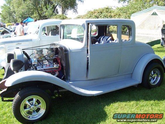 Gray hot rod coupe with exposed engine and chrome wheels, parked on grass