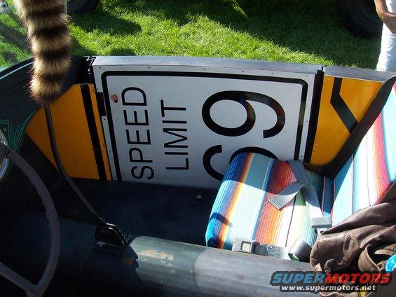 Car interior with a 'SPEED LIMIT 65' sign mounted behind the seats and a striped seat cover