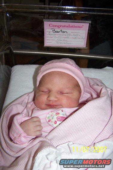 Newborn baby girl sleeping in a pink outfit and hat, with a 'Congratulations!' sign in the background. Date stamp shows 11/06/2007