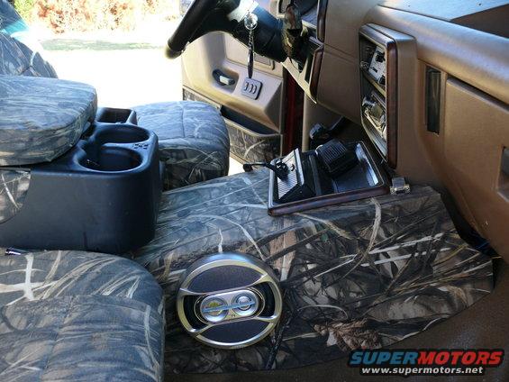 Interior of a vehicle with camouflage seat covers, a center console, and a speaker on the floor