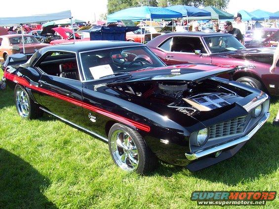 Black 1969 Camaro with red stripes, hood open showing engine, parked on grass at car show