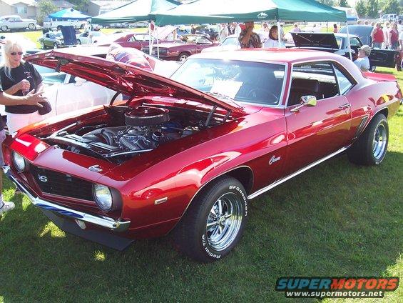 Red 1969 Camaro SS coupe with hood open, showing engine. People and other cars in background at an outdoor car show