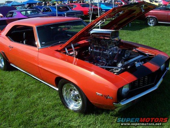 1969 Chevrolet Camaro Z/28, orange with black stripes, hood open showing supercharged engine. Other cars visible in background