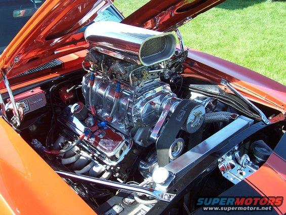 Orange car engine bay with a large chrome supercharger and scoop