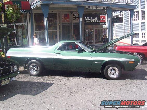Green 1972 Ford Ranchero parked on street, hood up, next to a red vehicle