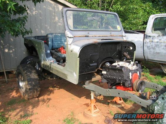 1980 Jeep CJ7 body on jack stands, engine out, next to a pickup truck