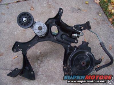 Power steering pump and pulley assembly on a black metal bracket, lying on concrete