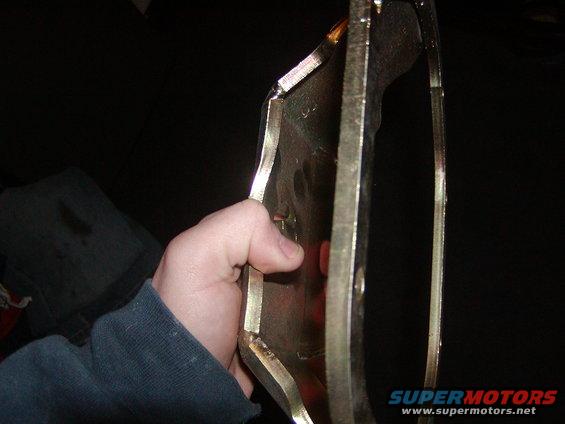 Hand holding a metallic automotive part against a dark background