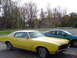 1972 Oldsmobile Cutlass - A yellow 1972 Oldsmobile Cutlass coupe is parked next to a green sedan on a street.