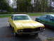 1972 Oldsmobile Cutlass - A yellow 1972 Oldsmobile Cutlass coupe is parked on a street, with a green sedan beside it.