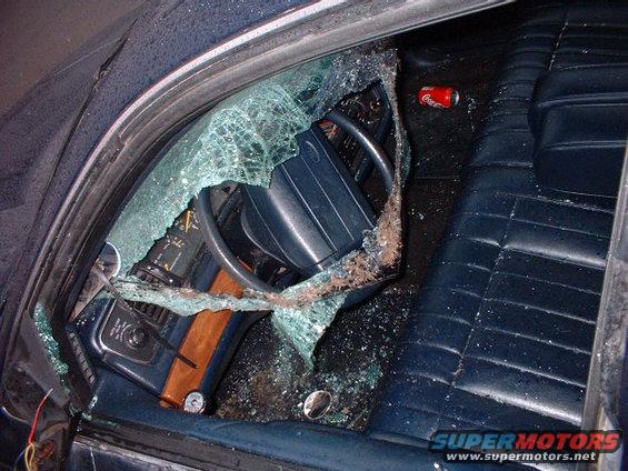 Dark blue interior of a 1996 Ford Crown Victoria with shattered driver's side window and debris on the dashboard and seats