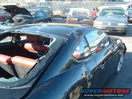 Black 2007 Hyundai Tiburon with shattered rear window and dented rear quarter panel, parked in a lot with other cars