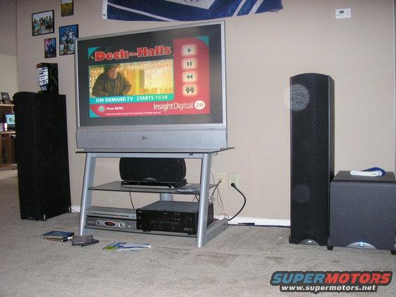 Television screen displaying 'Deck the Halls' on demand TV, with surround sound speakers and media console