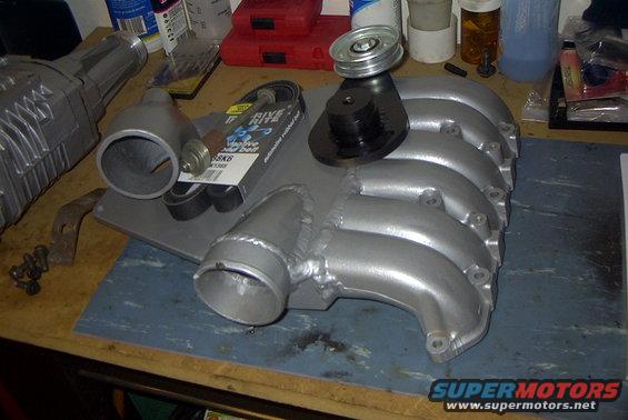 Supercharger, intake manifold, pulley, and belts on a workbench