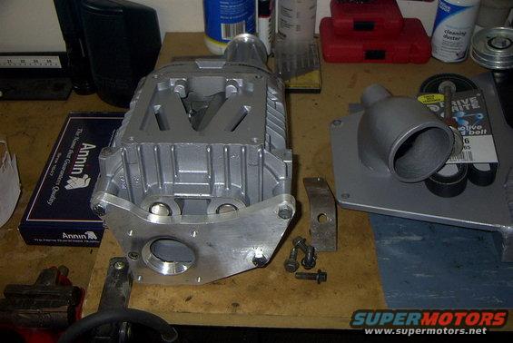Silver supercharger assembly with intake adapter and drive belt on a workbench