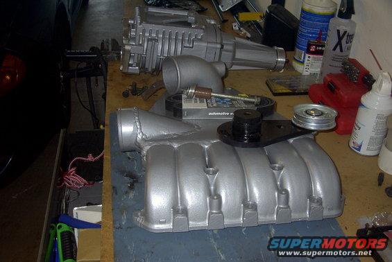 Supercharger and intake manifold parts on a workbench with tools and bottles