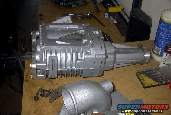 Silver supercharger and intake manifold on a workbench with tools and a bottle of fluid