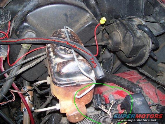 Close-up of brake master cylinder and associated hoses and wiring in engine bay. Text 'THIS' is written on a hose