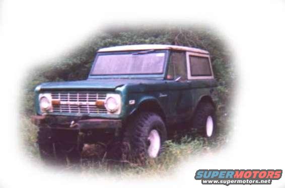 Green 1973 Ford Bronco with a white hardtop, parked outdoors in grass
