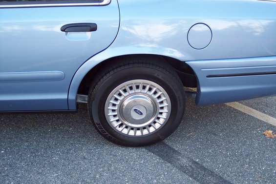 Light blue 2001 Ford Crown Victoria rear side view showing wheel, door handle, and fuel door