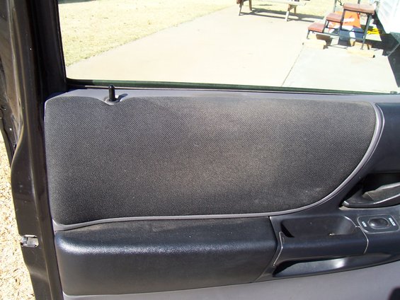 Black fabric door panel with silver trim and black armrest, viewed from inside a vehicle