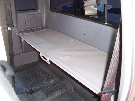 Interior of a truck cab showing a fold-down shelf above rubber floor mats and a seatbelt