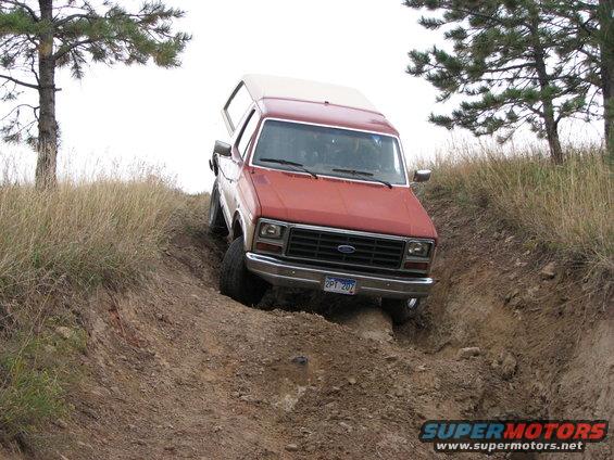 Red pickup truck with camper shell going down a dirt hill. License plate reads 2PT 207