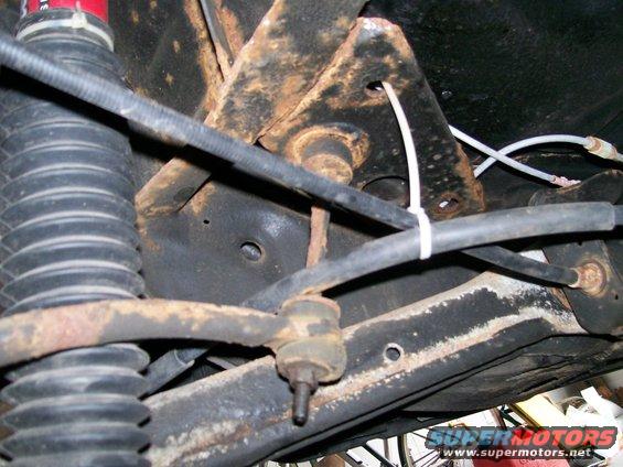 Underside view of rusty suspension parts, including a shock absorber and sway bar linkage