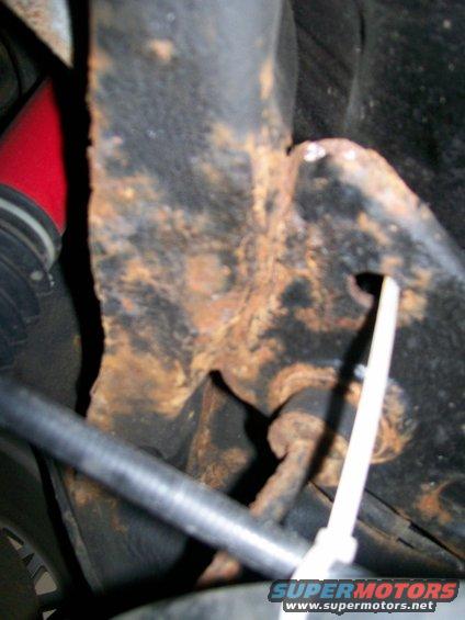 Rusted metal suspension part with a red hose and black tubing, secured by a white zip tie