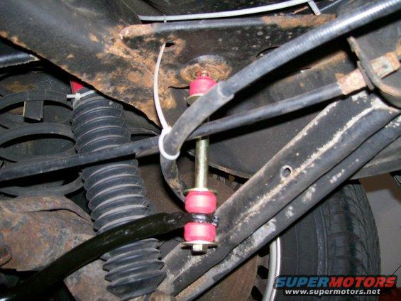 Rear sway bar with red bushings and yellow bolt, attached to rusty frame and black coil spring
