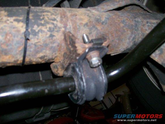 Close-up of a rusty rear sway bar mount with a black rubber bushing and a bolt