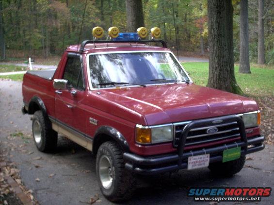 Red pickup truck with smiley face lights on roof rack, bull bar, and firefighter license plate
