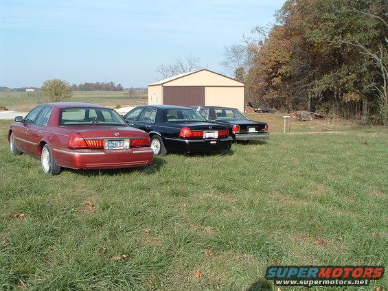Three Mercury Grand Marquis sedans parked in a grassy area with a barn in the background