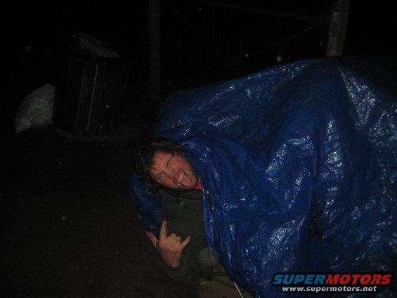 Person making a rock-on hand gesture and sticking out their tongue while under a blue tarp