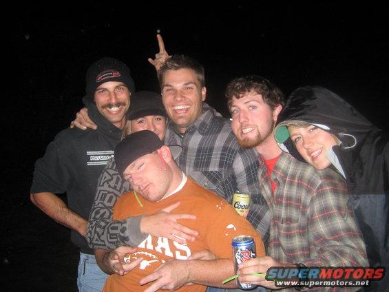 Group of six people posing for a photo at night. One person is asleep on another's shoulder