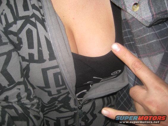 Person in a grey zip-up hoodie with a black tank top, showing cleavage. A hand is pointing
