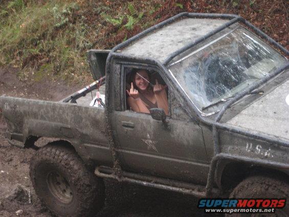 Mud-covered pickup truck with a roll cage and a person giving the finger