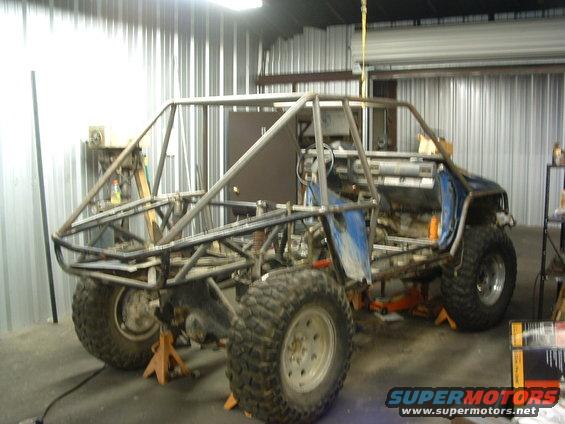 Custom off-road vehicle with roll cage, stripped interior, and large tires on jack stands