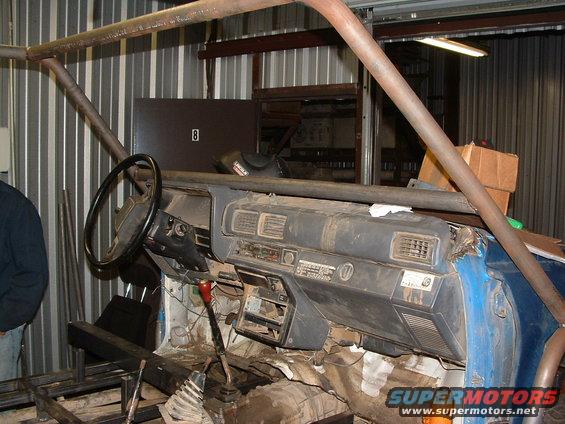 Interior of a blue vehicle with a roll cage, showing the dashboard, steering wheel, and gear shifter