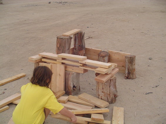 Child in yellow shirt building with wood blocks and logs outdoors