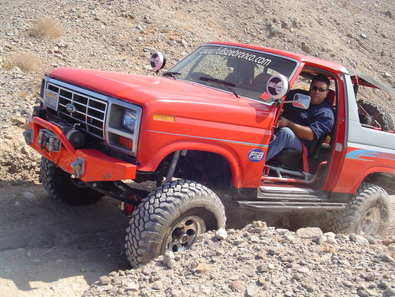 Red off-road SUV with custom bumper and winch, driving on rocky terrain