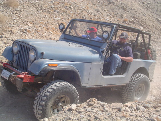 Blue Jeep CJ-7 with off-road tires navigating rocky terrain