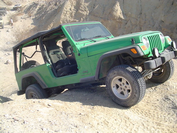 Green Jeep Wrangler going up a sandy hill, tires digging in. Another Jeep is visible further up the trail