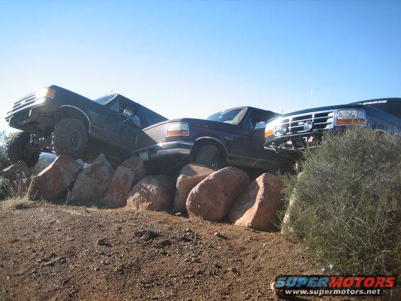 Three trucks, including a 1995 Ford Bronco, are positioned on large rocks