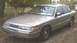 1994 Ford Crown Victoria - A silver 1994 Ford Crown Victoria is parked on a dirt lot with trees in the background.