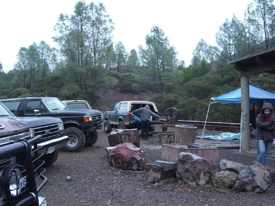 Several Ford Broncos parked at a campsite with trees and a picnic area