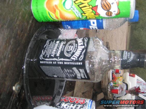 Jack Daniels bottle and cans on a surface with a white vehicle part in the background