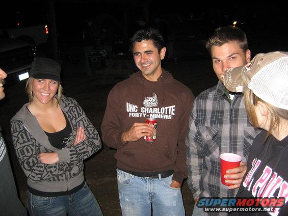 People gathered at night, one man wears a UNC Charlotte hoodie, another a plaid shirt