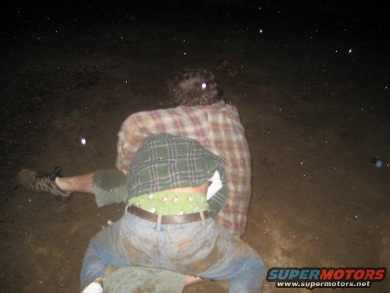 Two people in plaid shirts in a muddy outdoor scene at night